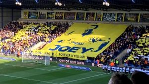 Oxford United supporters hold up a tifo banner reading Joey, Forever a Yellow, One of Our Own, in tribute to Joey Beauchamp at the Kassam Stadium